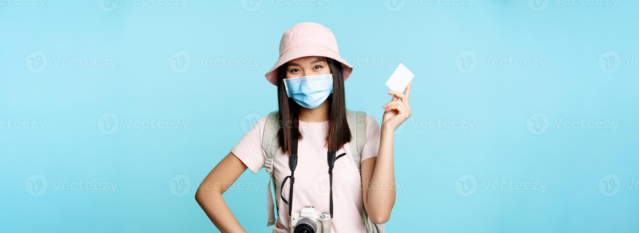 Happy korean tourist, girl on vacation standing with credit card and camera, paying for souvenirs, travelling abroad, standing over blue background photo