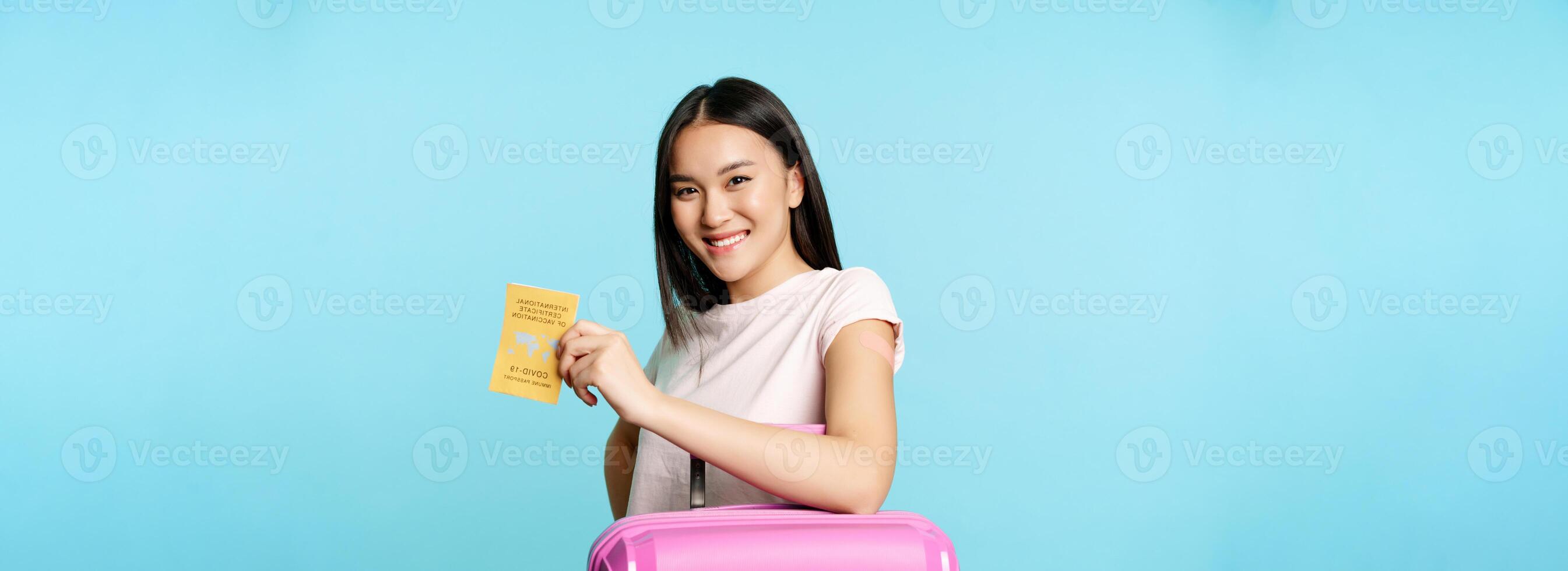 Happy smiling asian woman, tourist with suitcase showing international vaccination certificate from covid-19, getting vaccine from coronavirus for travelling abroad photo