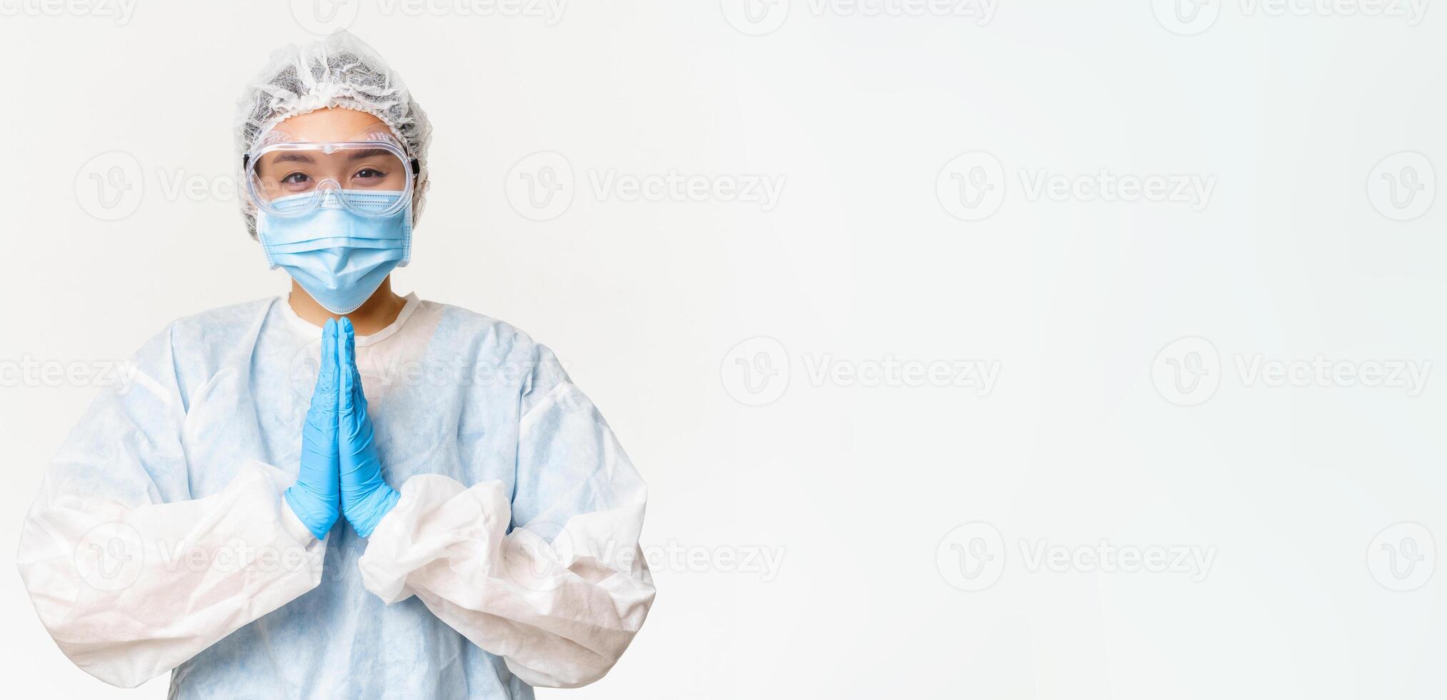 Please vaccinate. Smiling asian female doctor or nurse in personal protective equipment, showing beg, asking gesture, standing over white background photo