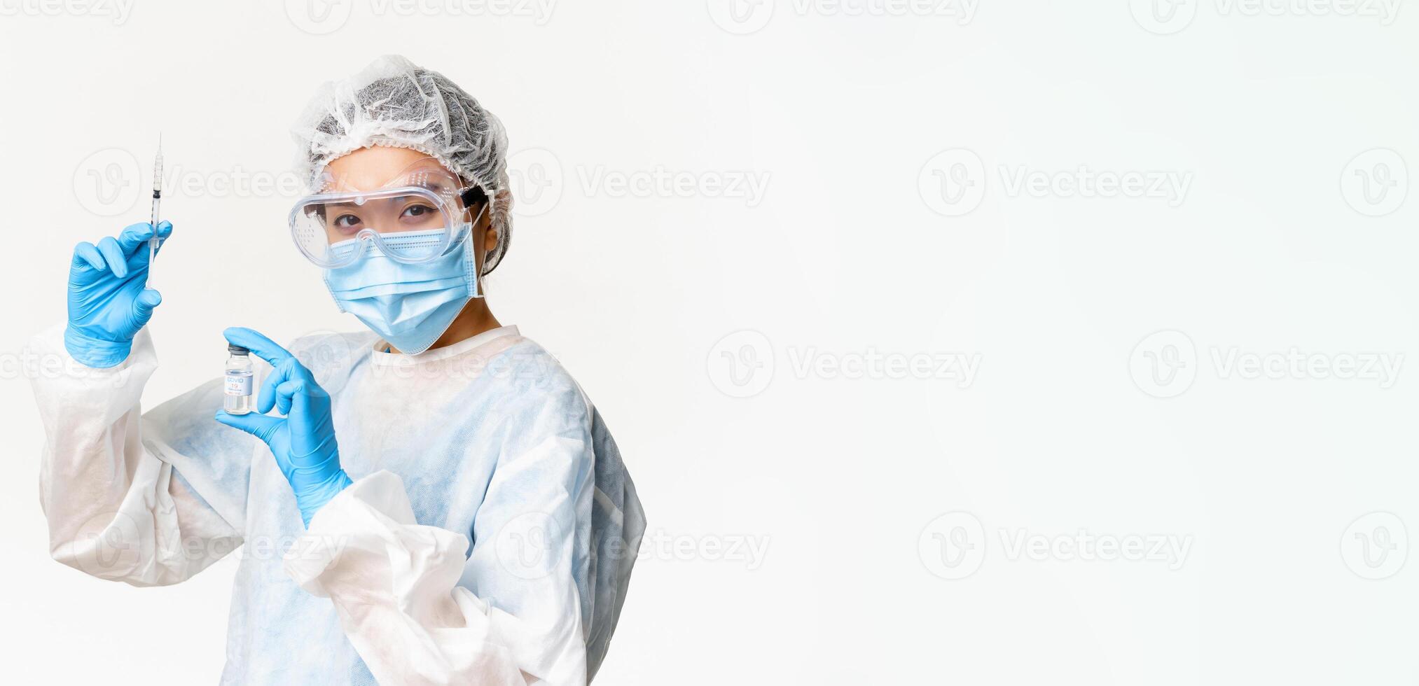 Asian doctor or nurse in medical protective equipment, looking confident at camera, holding syringe and vaccine from covid-19, vaccination campaign and medical concept photo