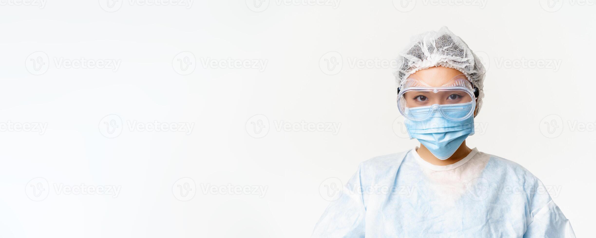 Asian female doctor or nurse wearing personal protective equipment with face medical mask and protective glasses, standing over white background photo