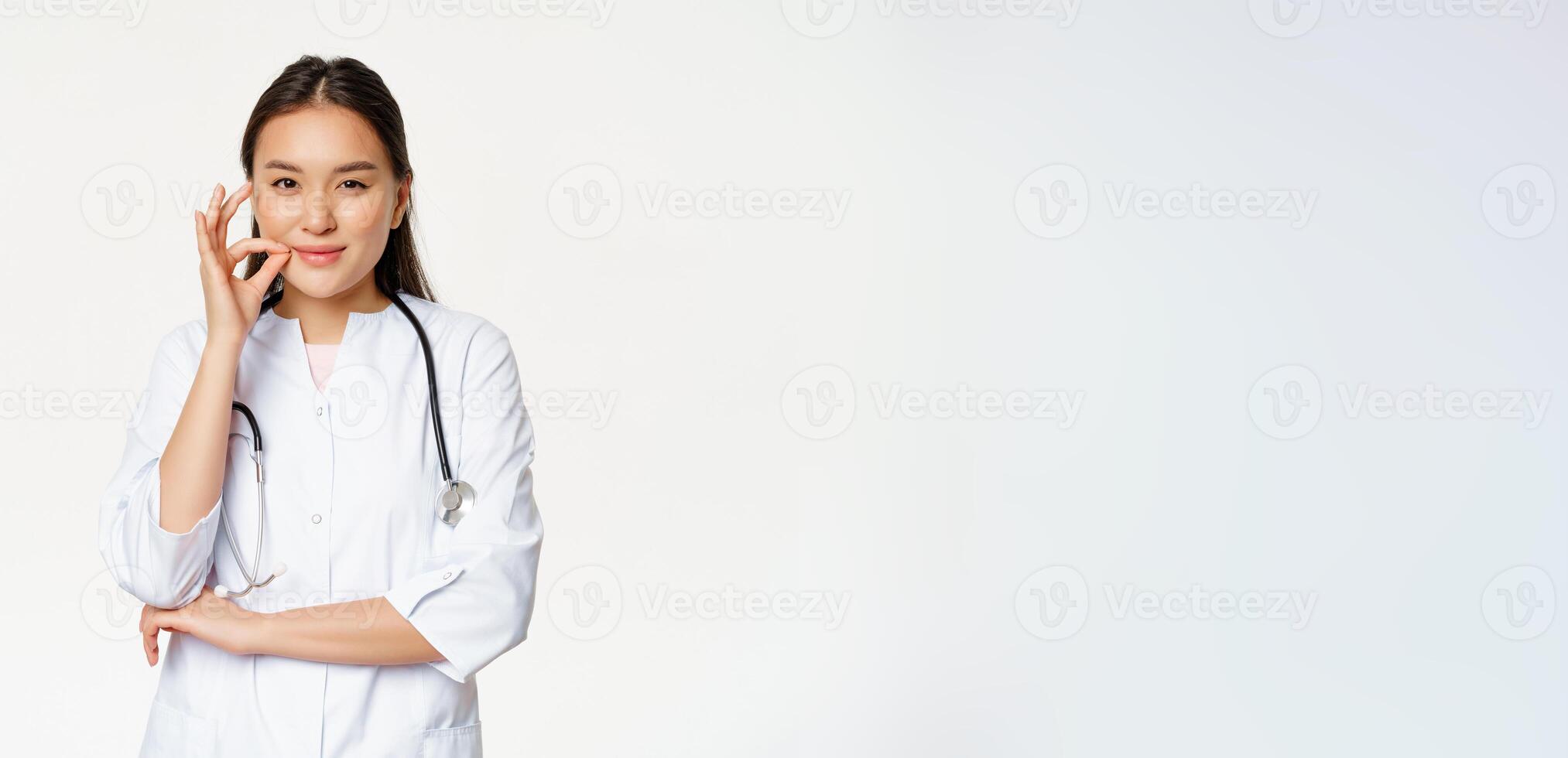 Taboo, medical confidentiality concept. Young asian doctor, female physician showing mouth silence, taboo or zip gesture, promise not tell, standing over white background photo