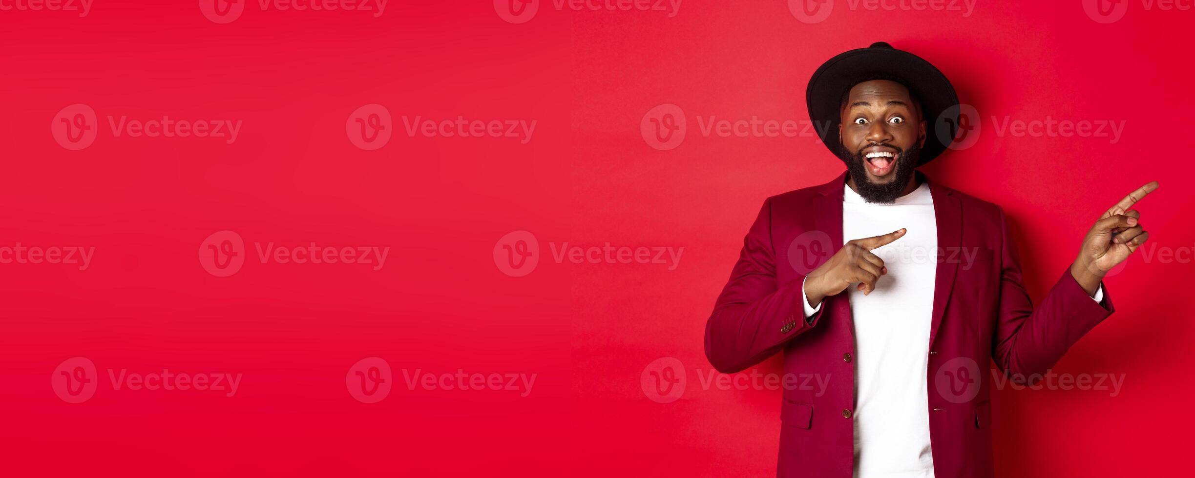 Winter holidays and shopping concept. Stylish african american man pointing fingers right at copy space for logo, standing over red background photo
