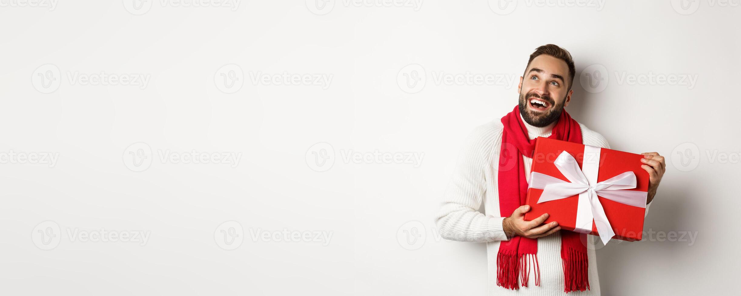 Merry Christmas. Happy man looking ecstatic and holding his New Year gift, standing against white background photo