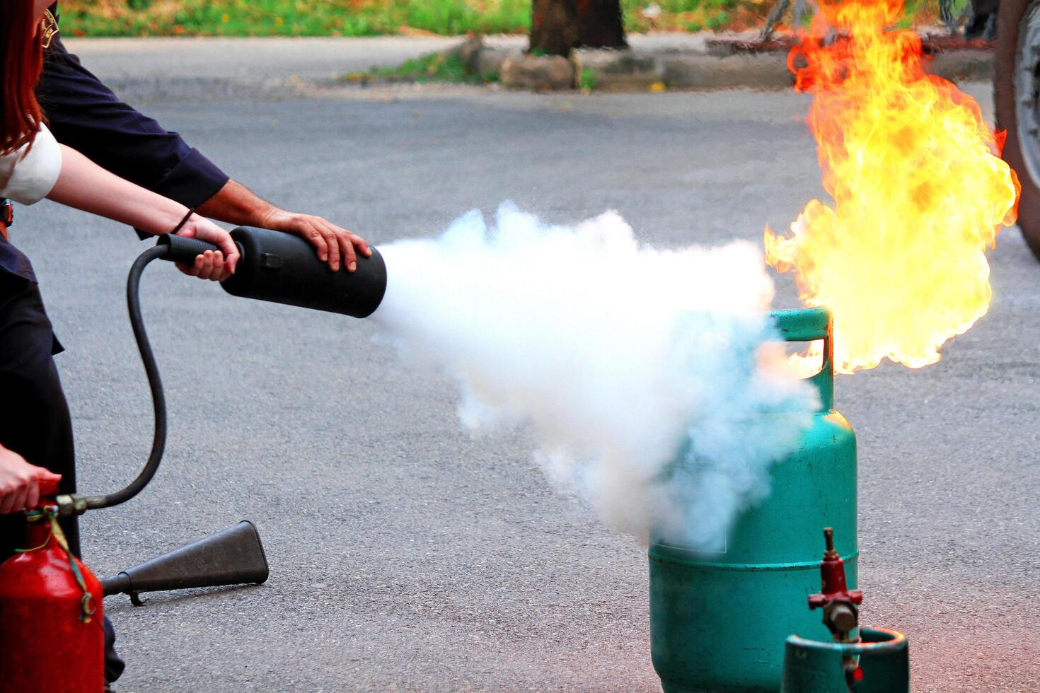 Firefighter teaching woman or man how to using fire extinguisher spraying foam to fire burning on gas container. Practice or Take Fire prevention course photo