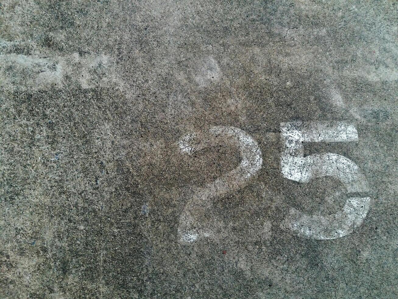 Number 25 or Twenty five number in white painted on the gray concrete wall or surface of street with copy space. Background concept photo