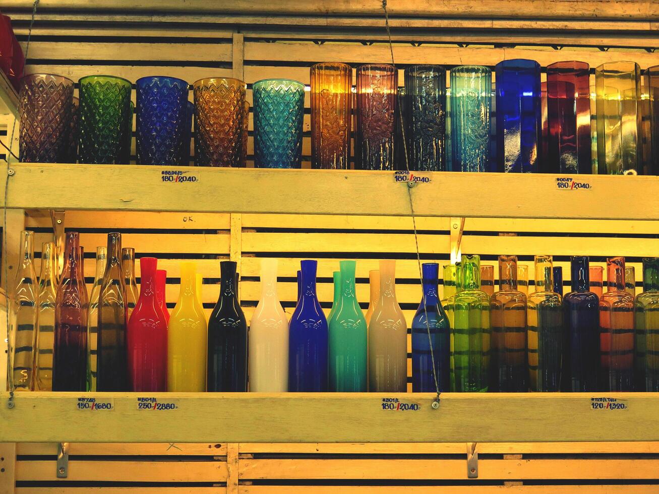 Colorful of glass, bottle and vase on wooden shelf for sale at dishware store or shop in yellow tone. Design object photo