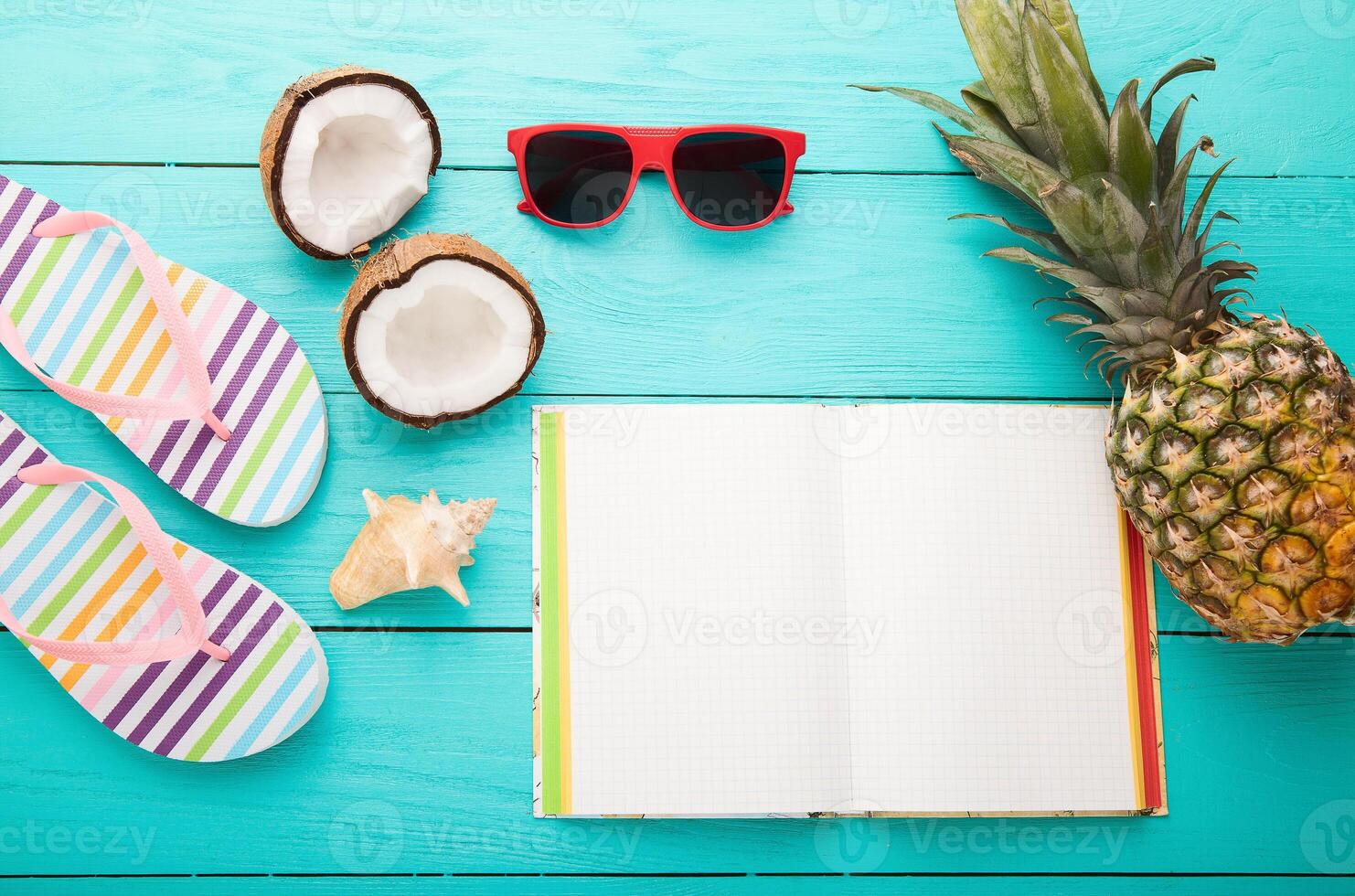 Tropical vacation concept with notebook, flip flops, coconut, pineapple, sunglasses, and coconut photo
