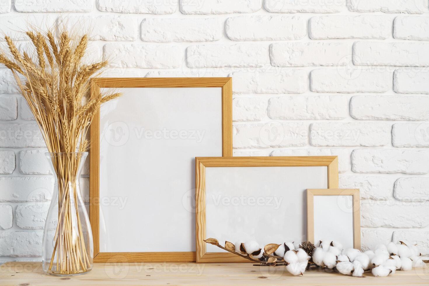Vase with ears of wheat and photo frames against brick wall