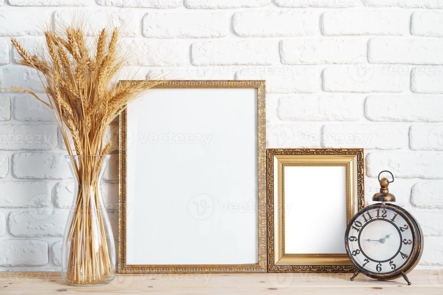 Vase with ears of wheat and photo frames against brick wall