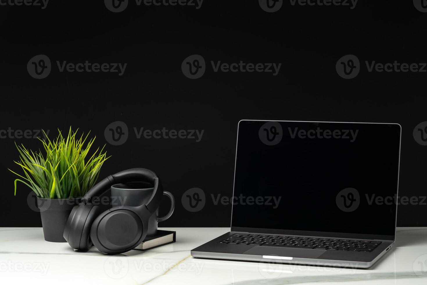 Laptop with black screen on working desk with cup and earphones on black background photo