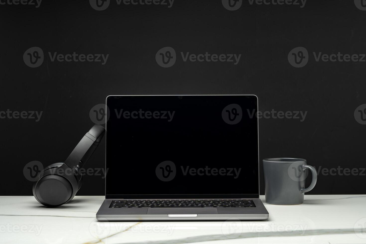 Laptop with black screen on working desk with cup and earphones on black background photo