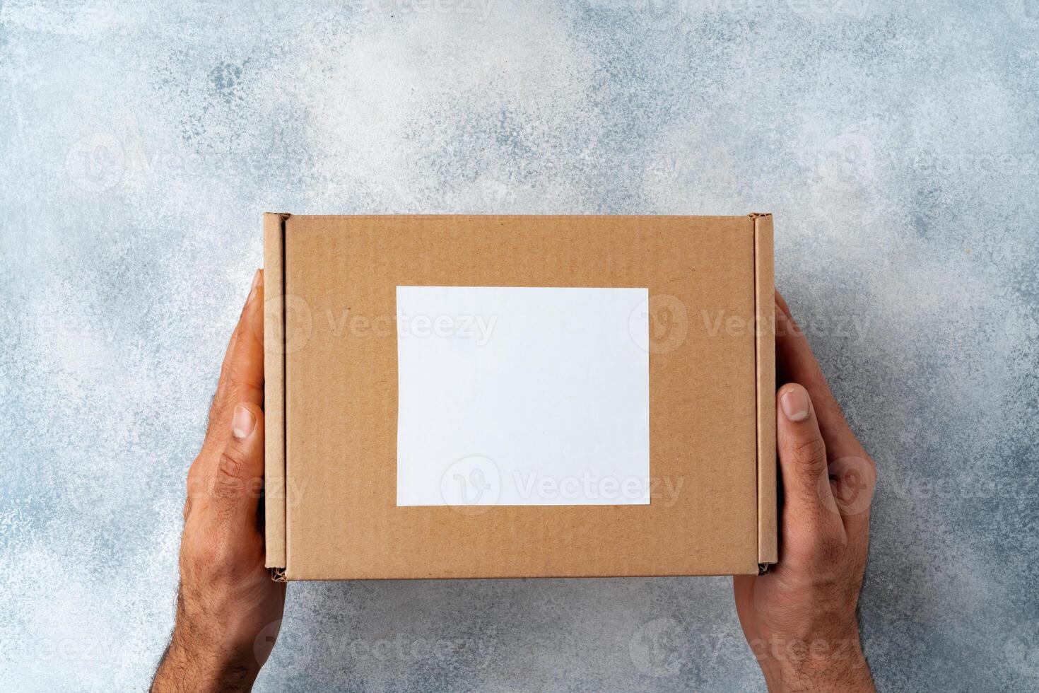 Parcel cardboard box in a man hands on a gray table background photo
