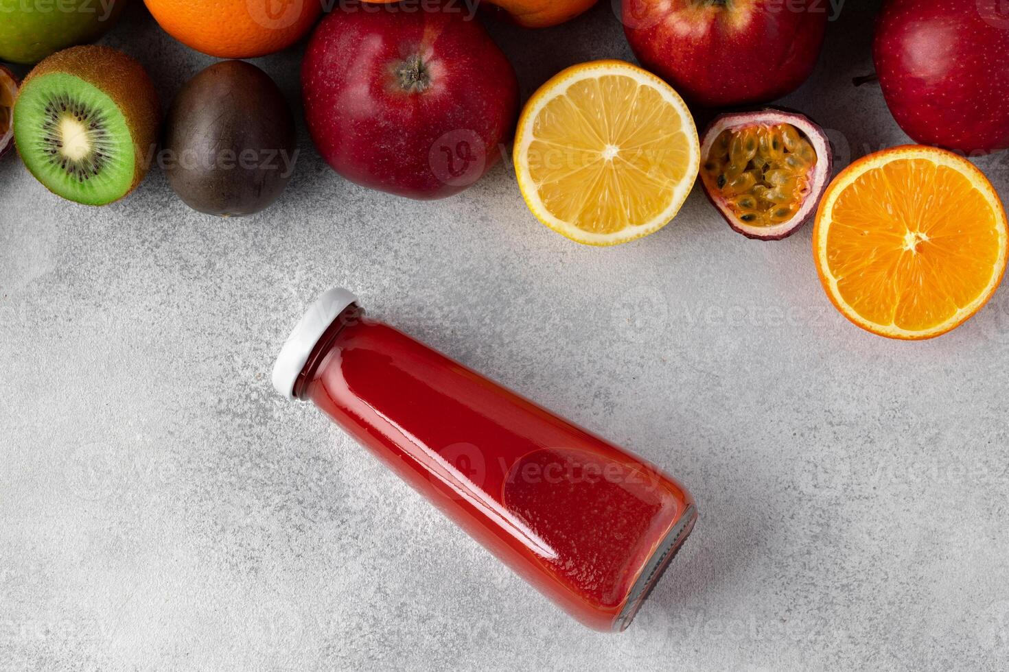 Various fruits and freshly squeezed fruits juice in bottle on gray background photo