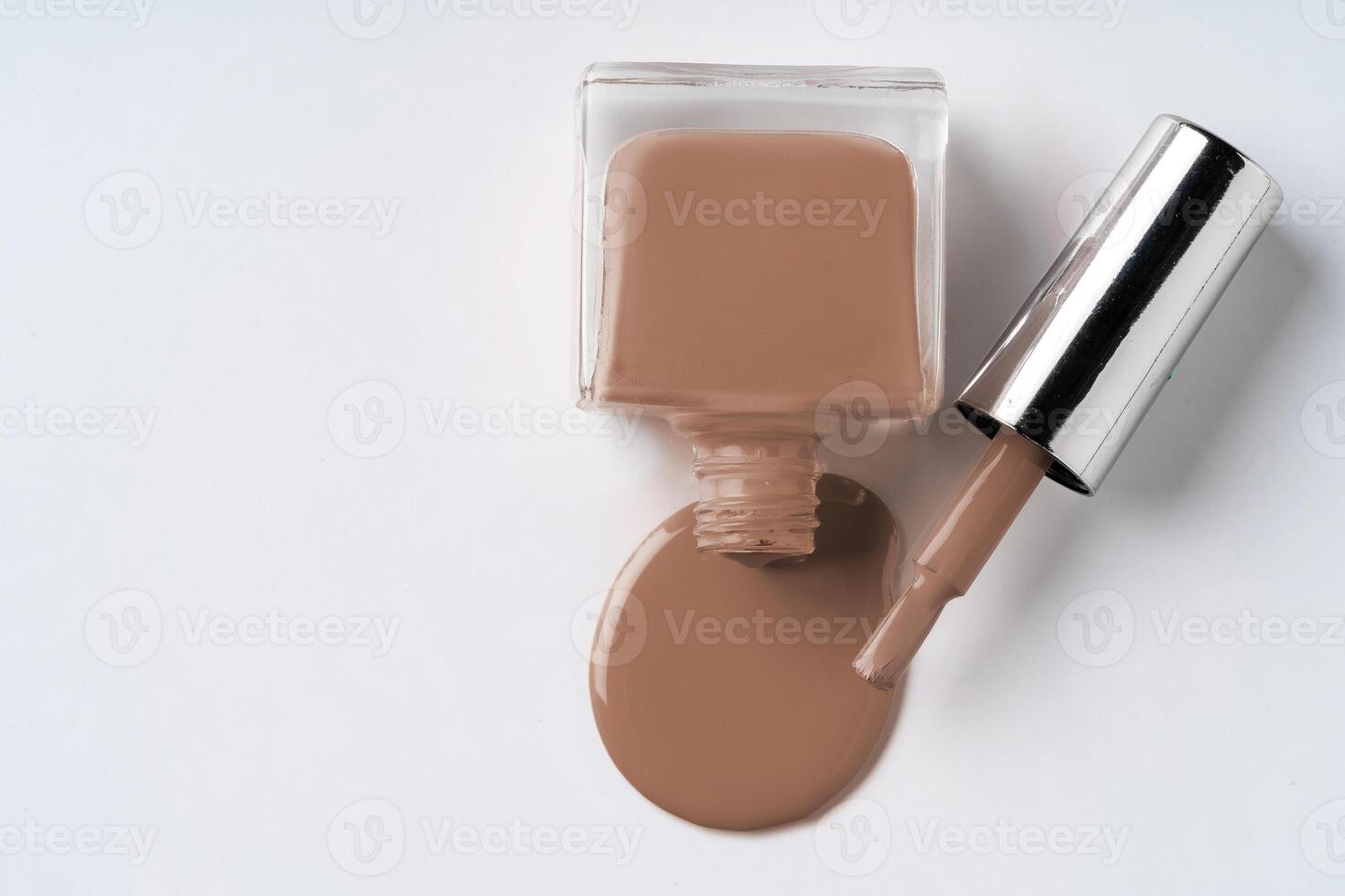 Nail polish bottle spilling soft beige polish onto a white surface in a minimalist setting during bright daylight photo