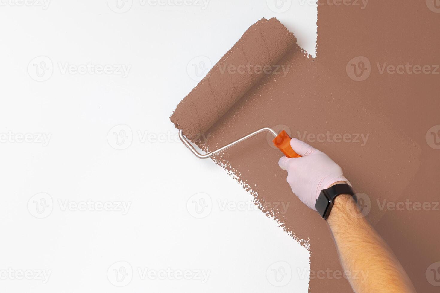 Person using a paint roller to apply brown paint to a wall in a well-lit room during a home improvement project photo