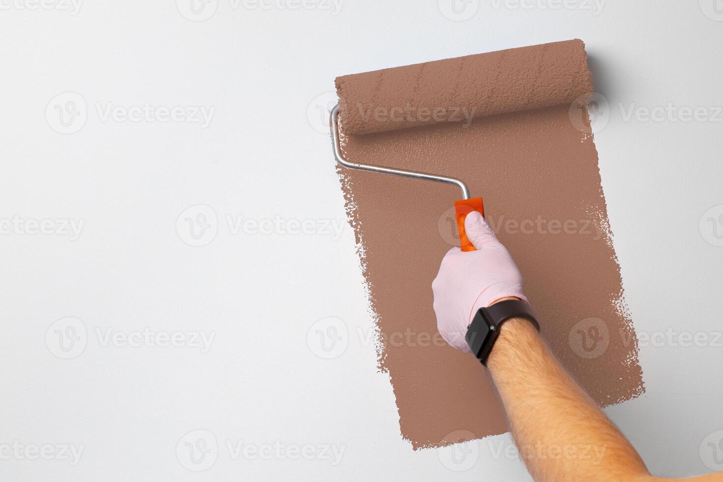 Individual painting a wall with a roller brush in a room, showcasing a brown color and a fresh look photo