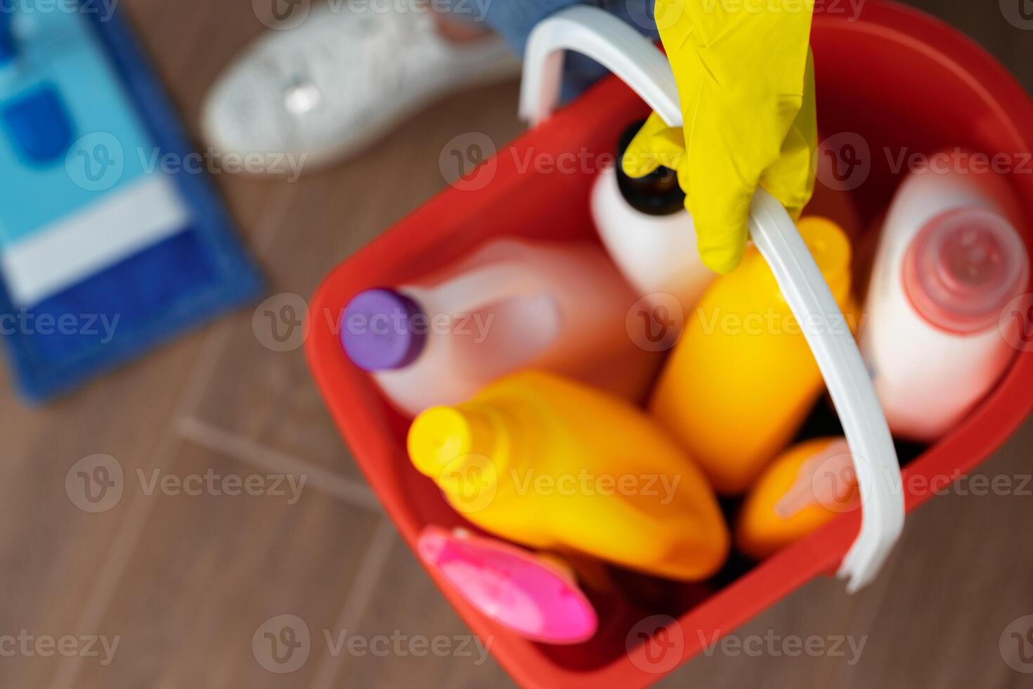 Various household cleaning detergents and bottles in a plastic bucket on the floor photo