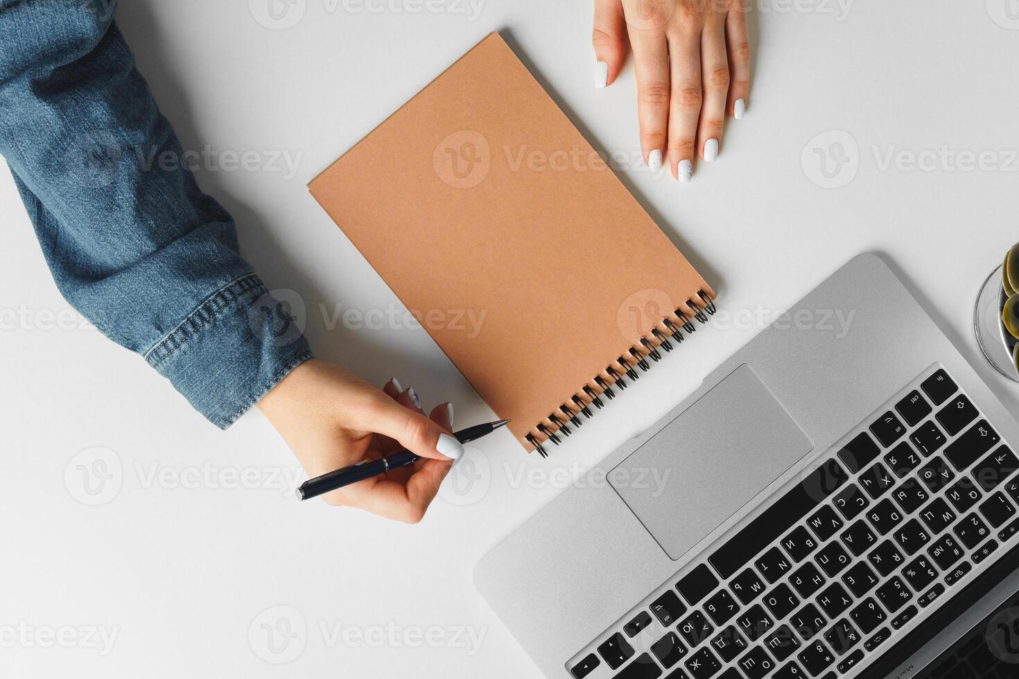 Female hand writing in a notebook on table with laptop, view from above photo