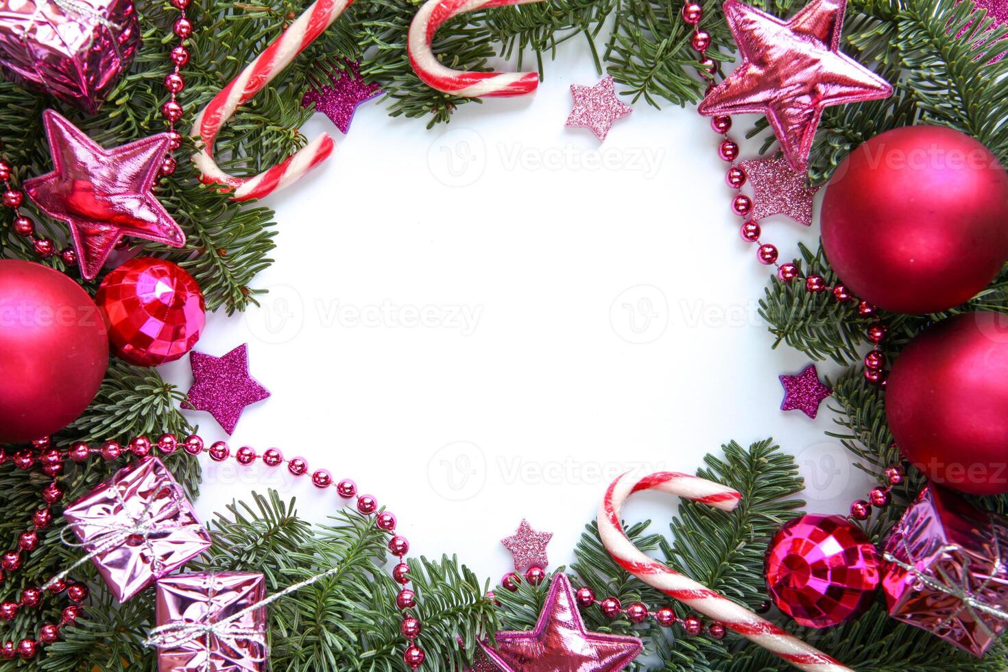 Vibrant Christmas-themed photograph features lush green fir branches adorned with fuchsia ornaments, candy canes, pink stars, shiny beads and small wrapped gifts, framing a blank white center for text photo