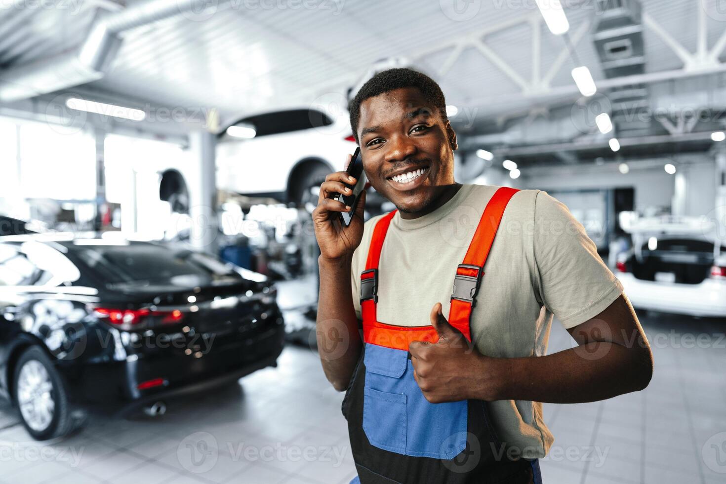 Young African mechanic man wearing uniform using mobile phone in a car service photo