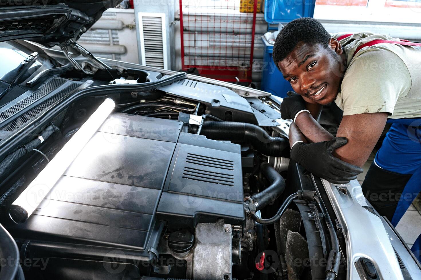 Young African man working under the hood of car fixing engine in auto service photo