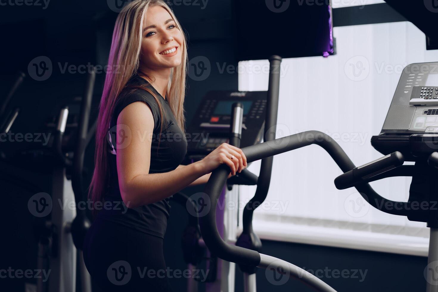 Attractive young blonde woman exercising on cardio training apparatus photo