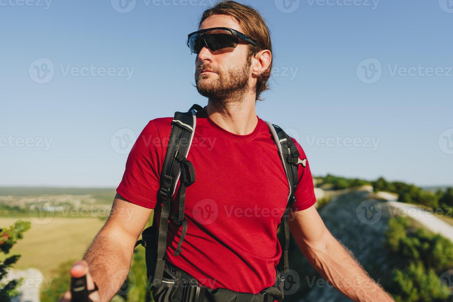 Bearded traveler with a backpack and sunglasses on the top of a mountain photo
