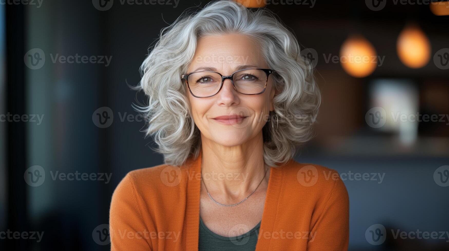 Smiling older woman with glasses wearing an orange sweater in a cozy indoor setting during the evening photo