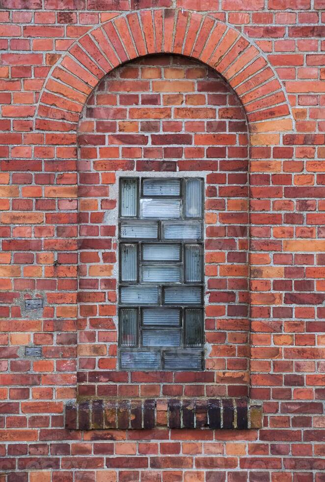 Arch in a wall made from red bricks with a small glass element photo