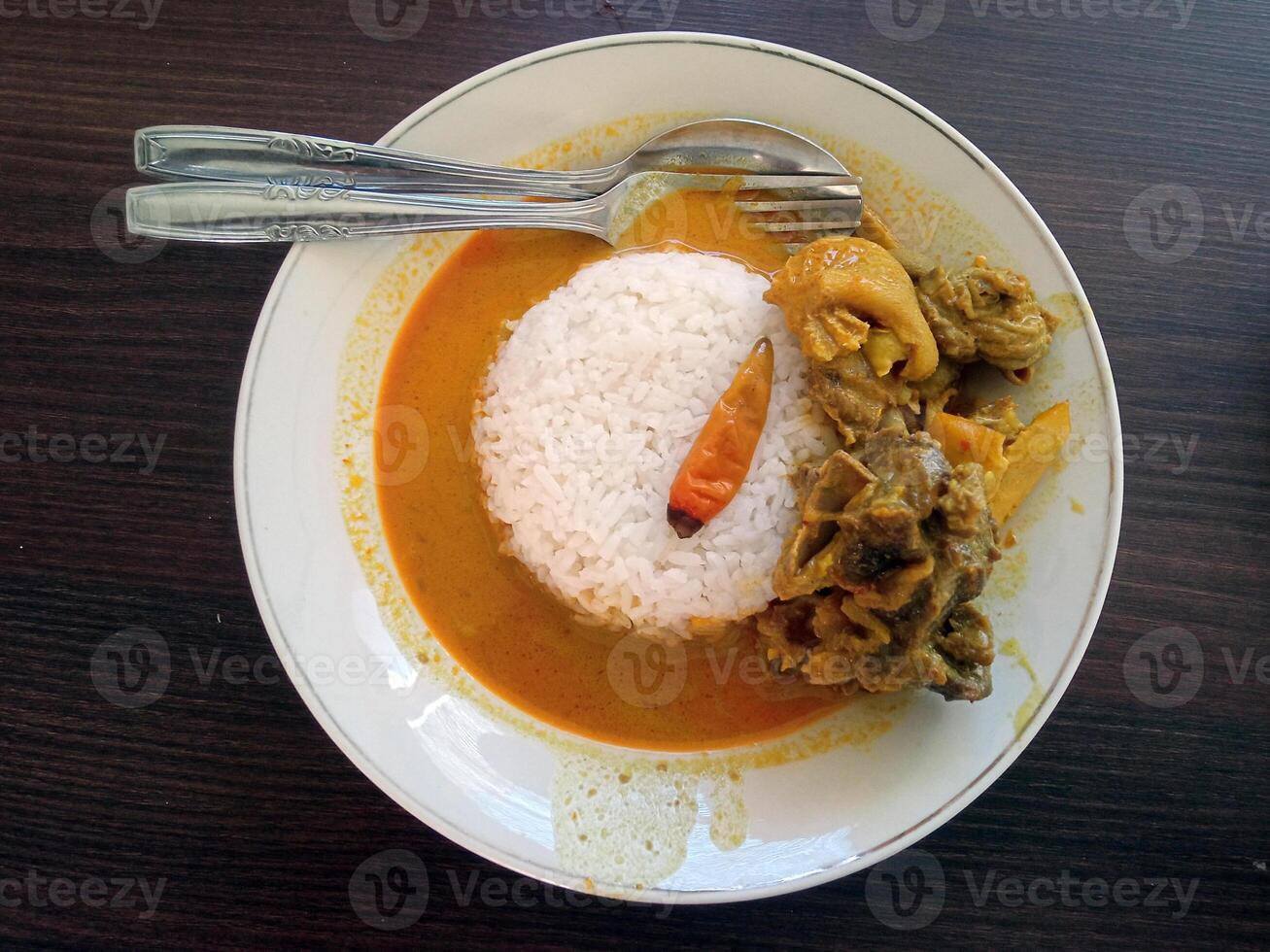 Flat lay view of A plate of rice with goat curry and a chili on a wooden table. An Indonesian traditional cuisine concept. photo