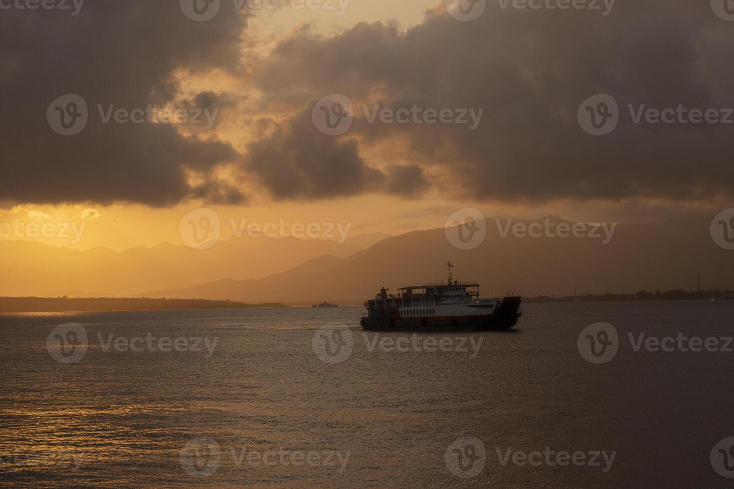 A passenger ship sailing in the Bali Strait with the background of the sunrise and the silhouette of mountain formations. photo
