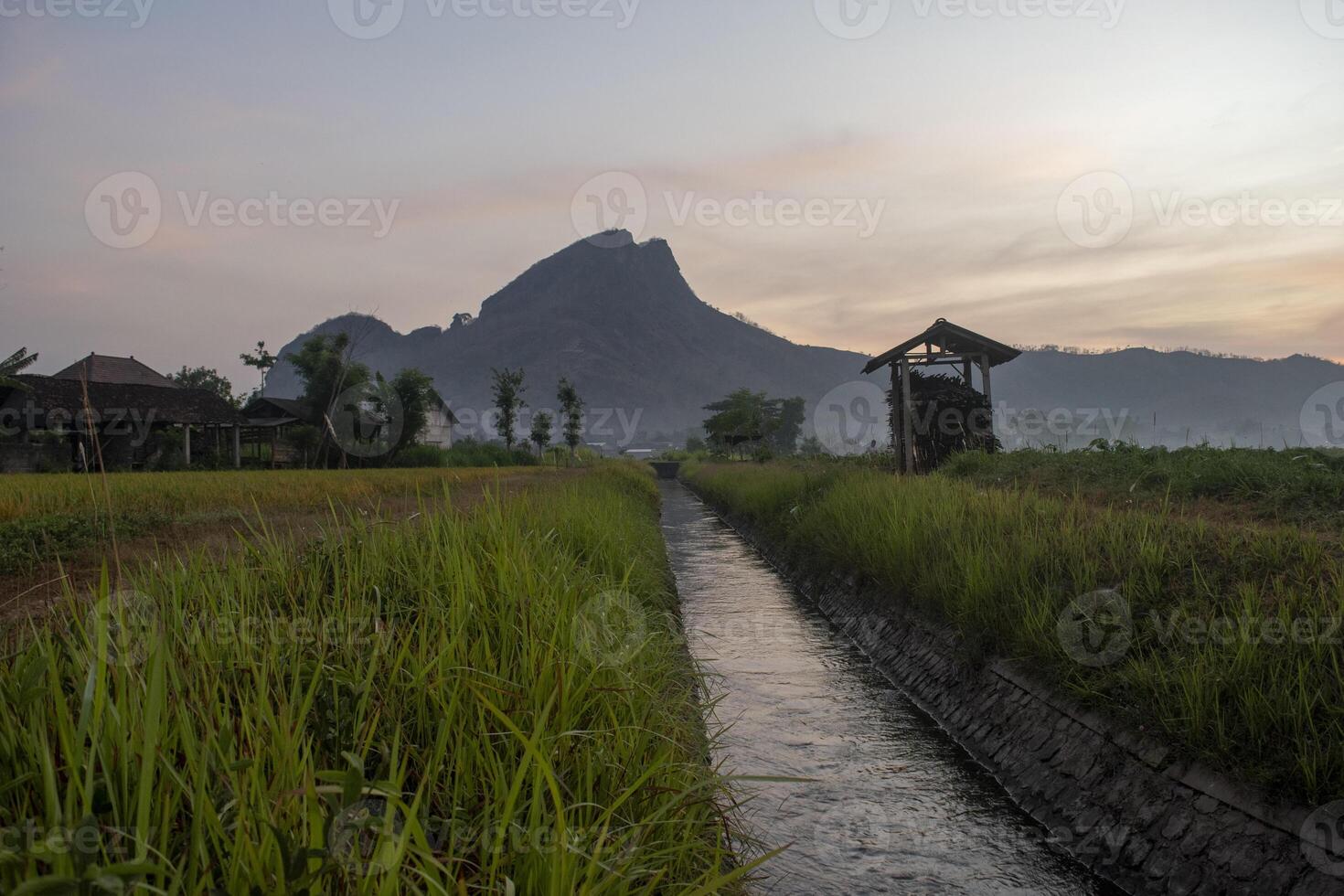 Morning vibes in the countryside with an irrigation canal and a mountain in the background. A serene atmosphere in agricultural field. photo