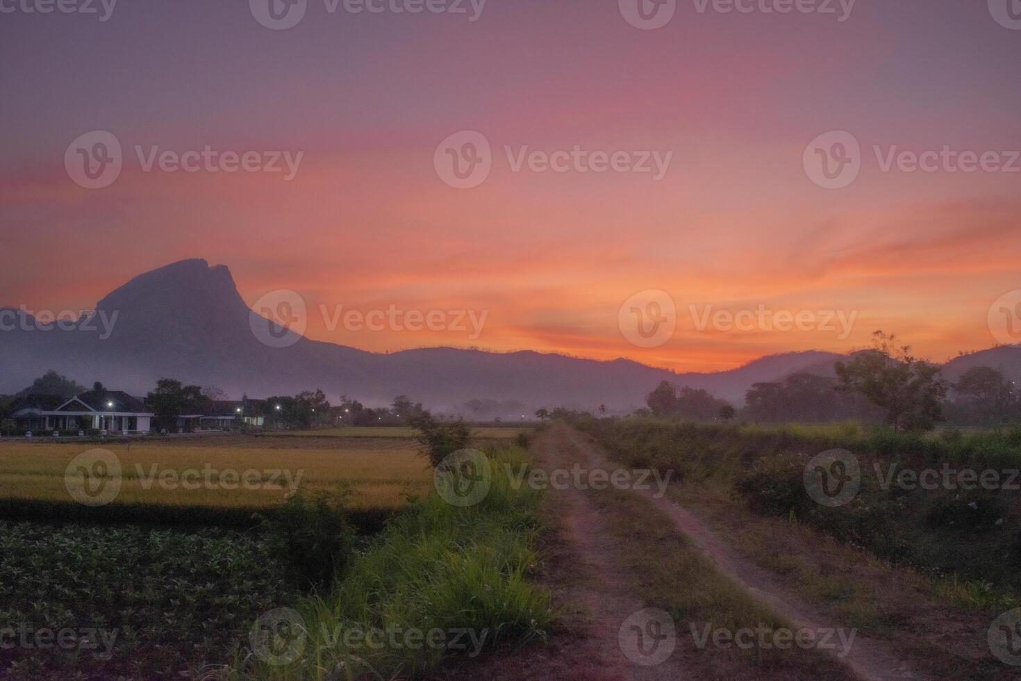 A pathway in the countryside with a mountain and red sky in the background photo