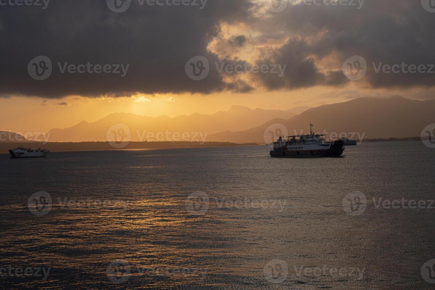 A passenger ship sailing in the Bali Strait with the cloudy sunrise and the silhouette of mountain formations in the background. photo