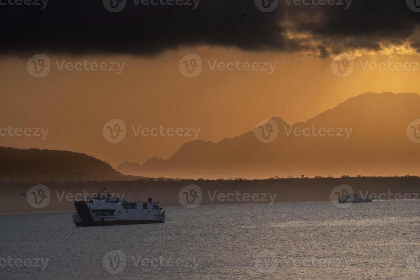 Two passenger ships sailing in the Bali Strait with the background of the cloudy sunrise and the silhouette of mountain formations. photo