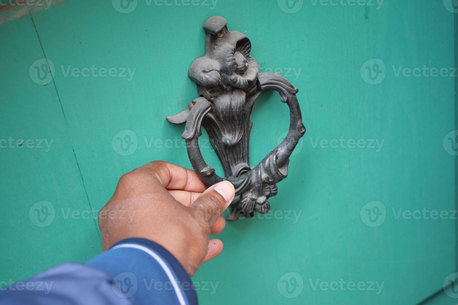 A hand reaching for a beautifully designed knocker on a green door photo