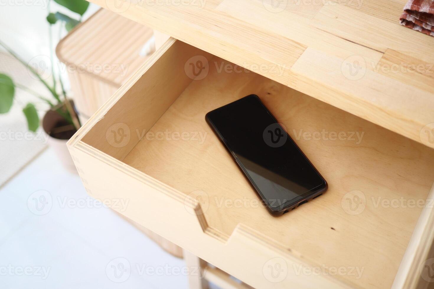 A sleek smartphone in a wooden drawer embodies modern minimalism photo