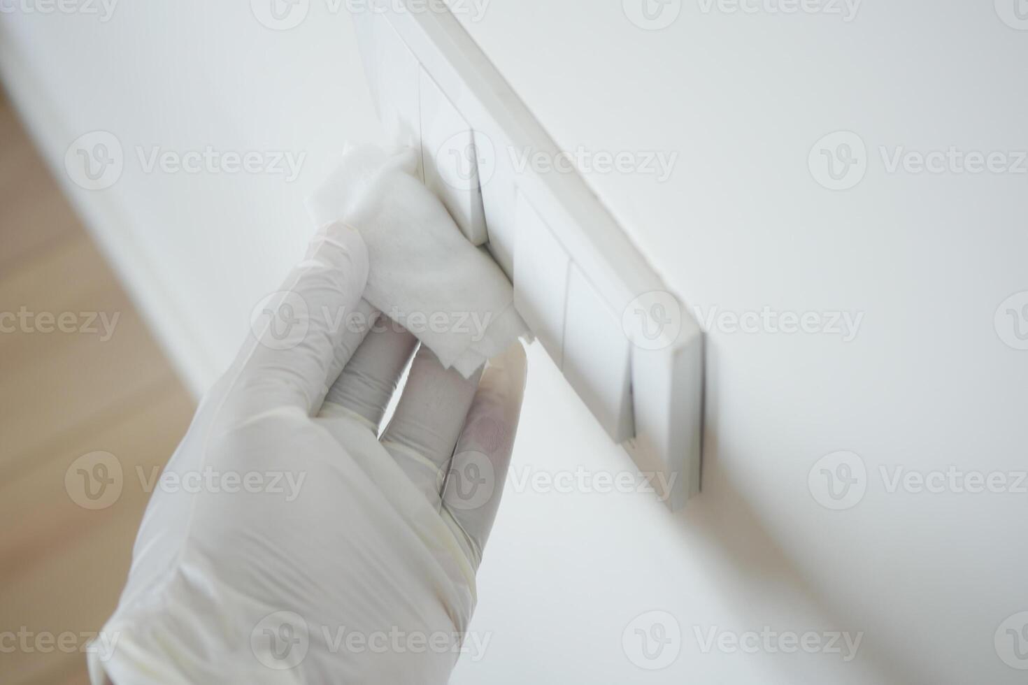 Using a gloved hand to carefully clean the wall switch thoroughly and safely photo