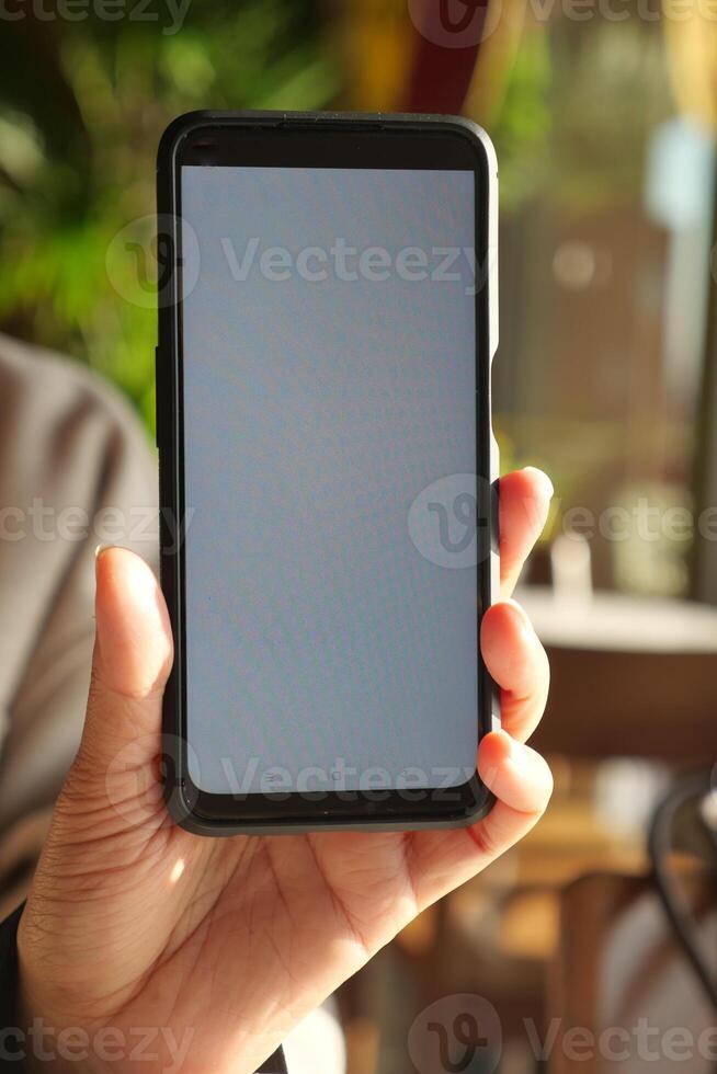 Individual Grasping Smartphone with a Blank Screen in a Cozy Cafe Environment photo