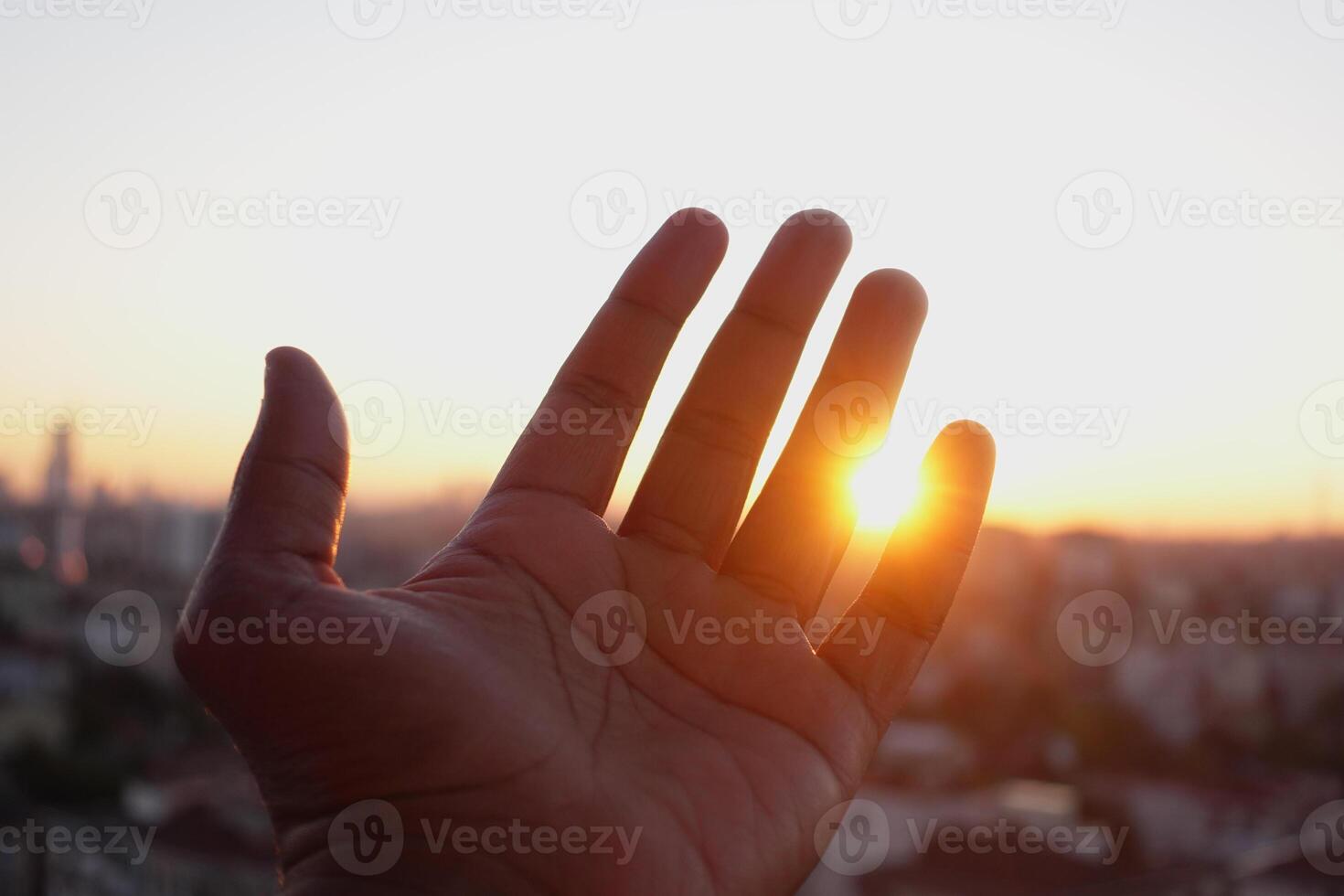 A Hand Extending Gracefully Towards the Bright Sunlight Shining Above the Urban Cityscape Below photo