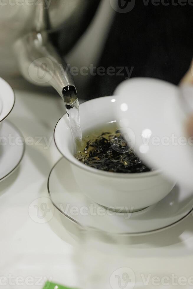 A teapot gracefully pouring aromatic tea into a pristine white ceramic cup for enjoyment photo