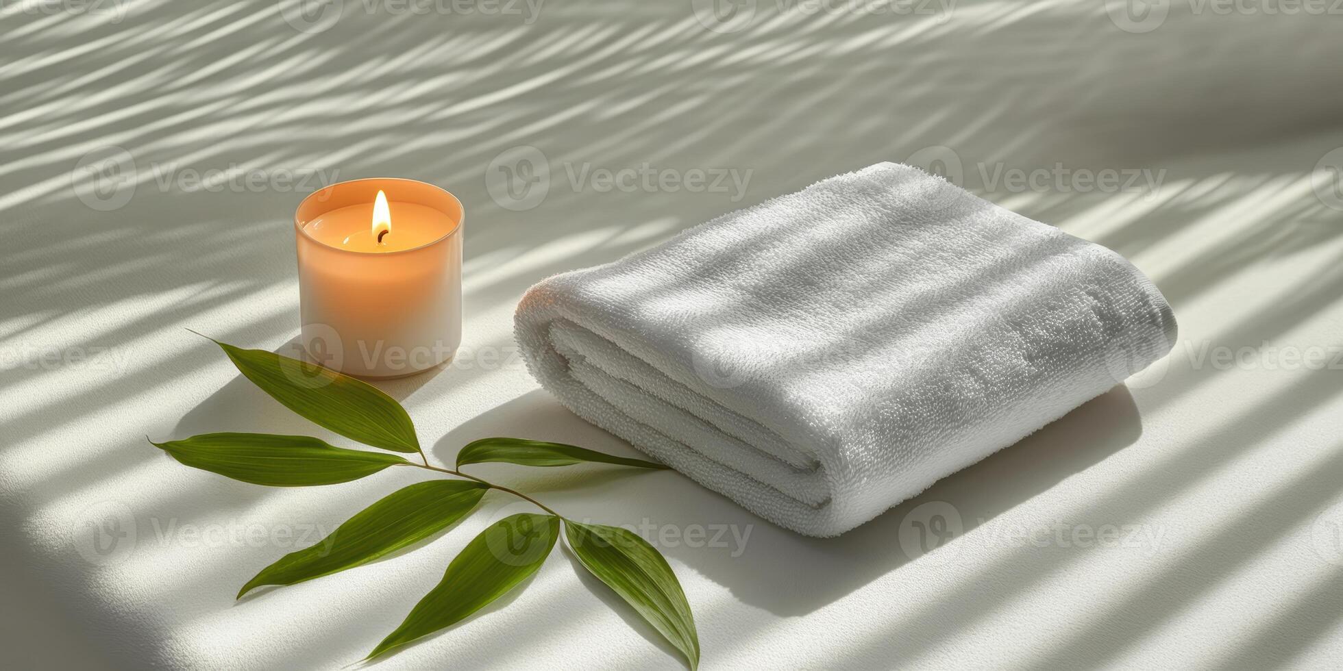 A rolled white towel, lit candle, and a single leaf placed on a spa bed photo