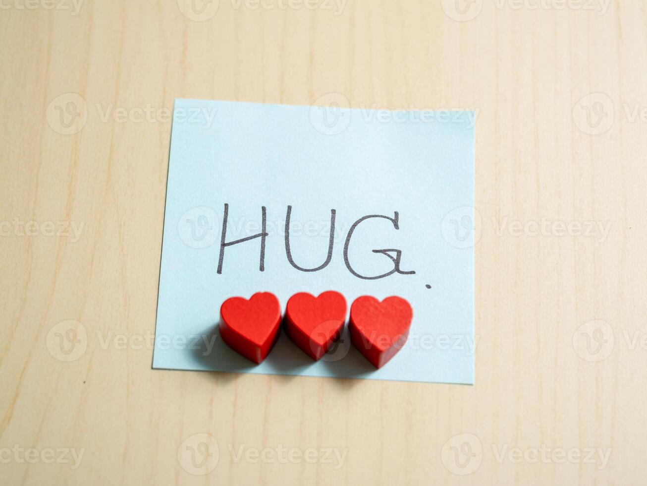 Close-up of heartfelt hug message with red hearts and blue note in warm atmosphere photo
