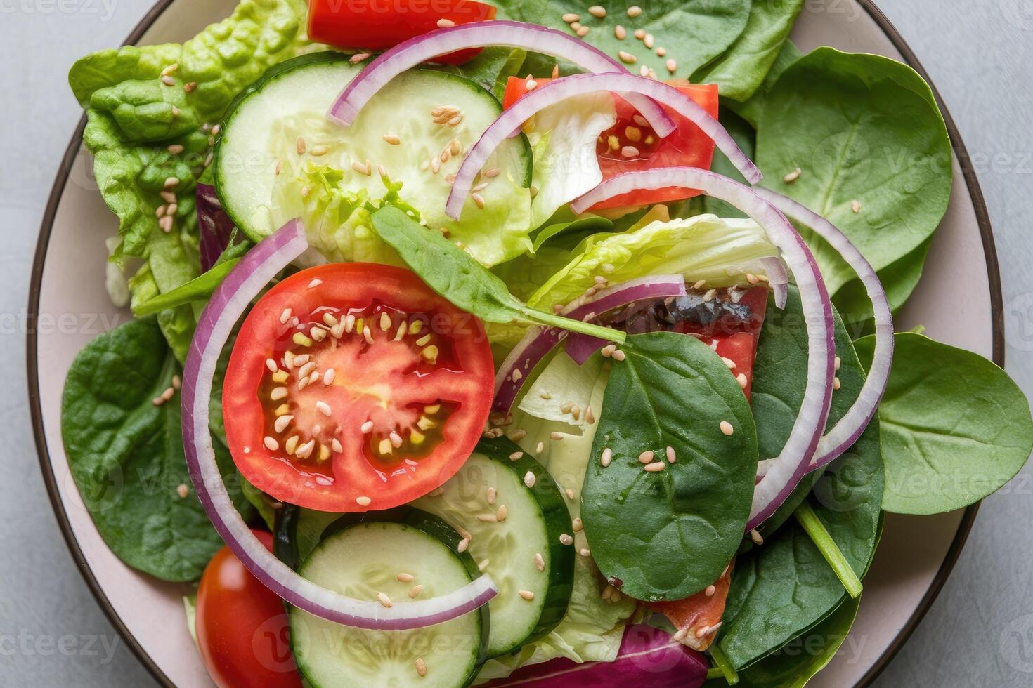 Fresh garden salad with tomatoes, cucumbers, onions, spinach, and sesame seeds on white plate photo
