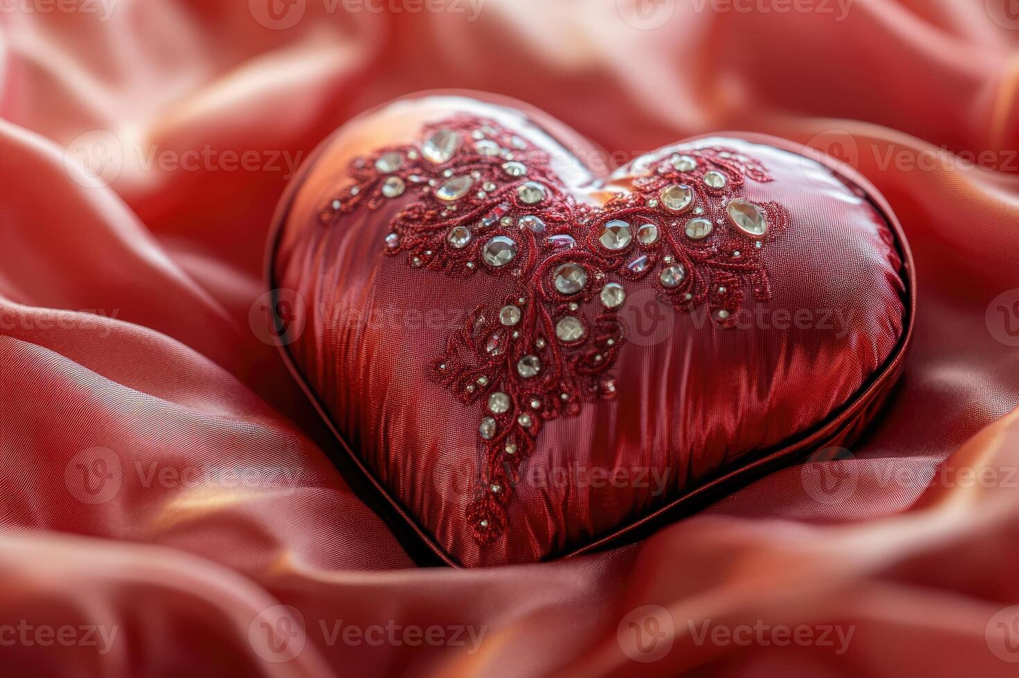 Red satin heart shaped gift box decorated with embroidery and rhinestones resting on silk fabric photo