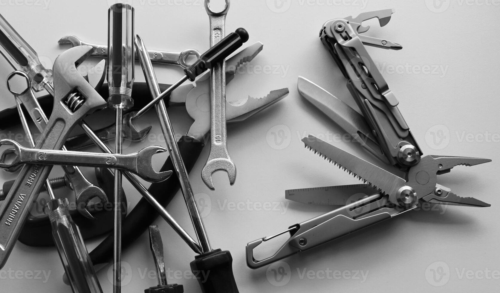 Black and white image of blades and screws of steel multi-tool VS pile of hand tools dumped in disarray photo