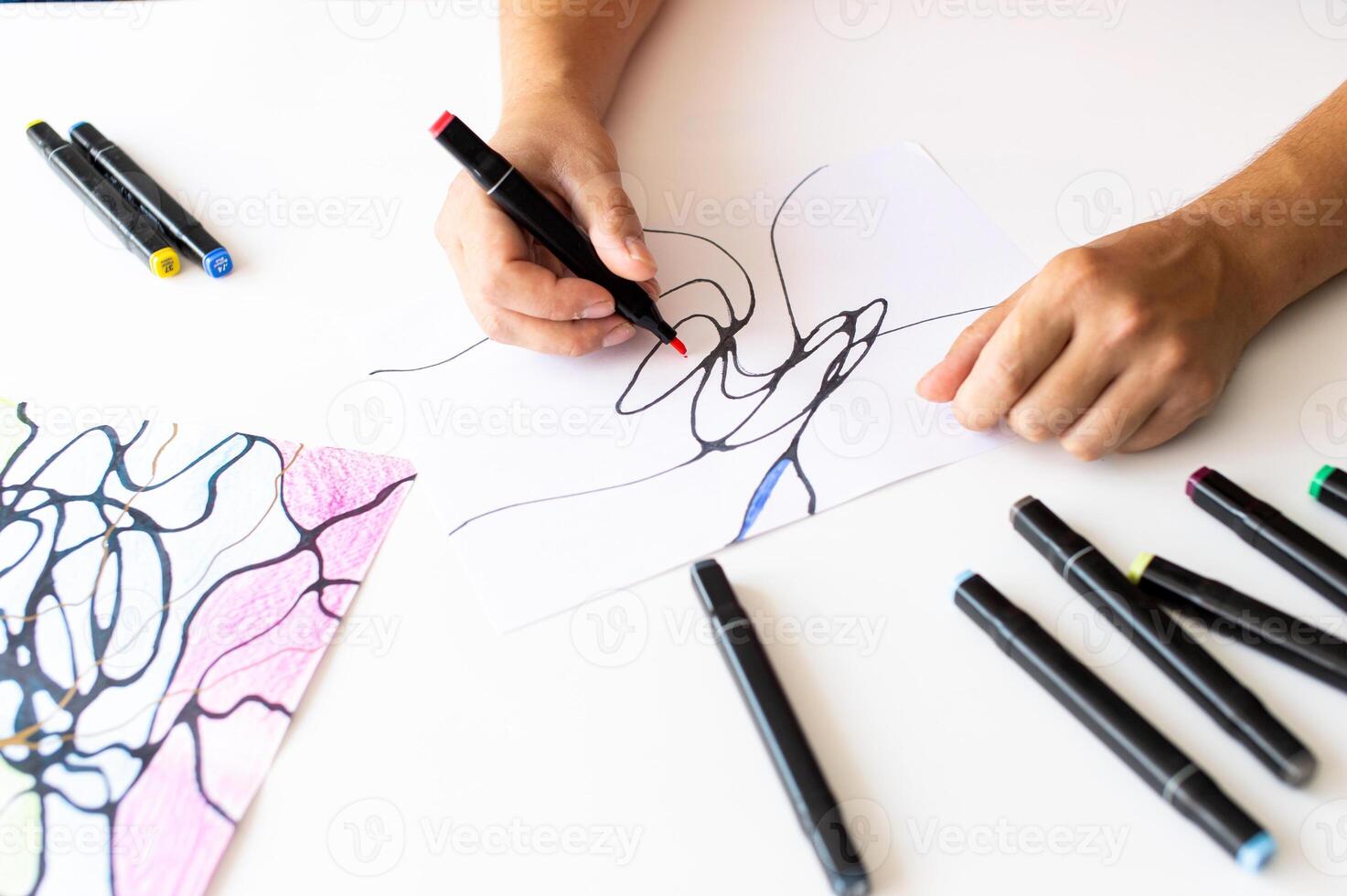 Person drawing abstract lines with a black marker on white paper. photo