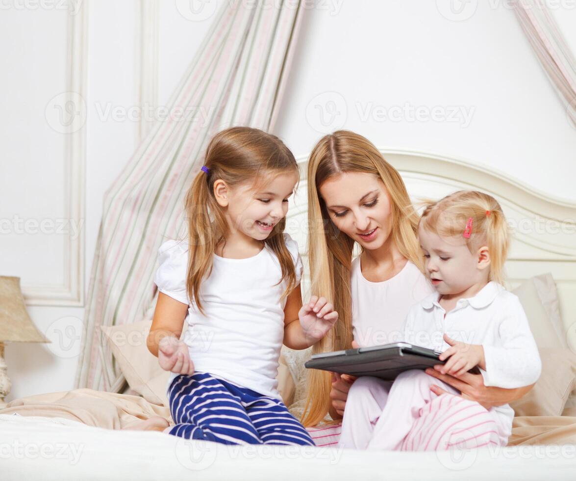 Happy mother and her little daughters having fun using a tablet computer photo