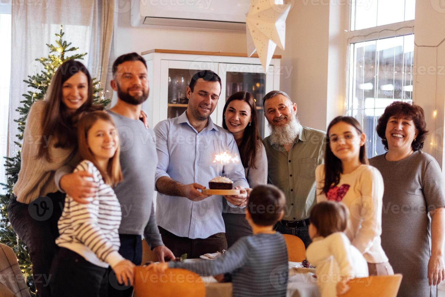 A big happy family at a festive table at home. An attractive young man with a cake with lighted sparklers and his smiling relatives in the living room. photo